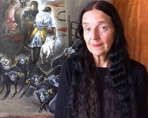 Color photograph of artist Sue Coe with a painting she created.